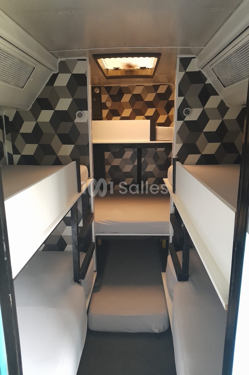 Intérieur d'un véhicule aménagé avec quatre lits superposés et un espace de rangement au fond, décor géométrique.