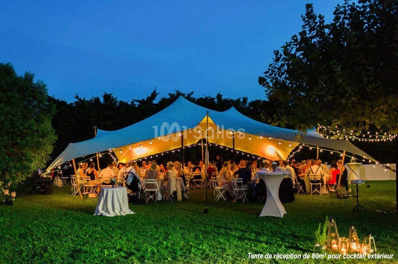 Tente éclairée abritant des invités assis à des tables lors d'une réception en soirée dans un jardin.