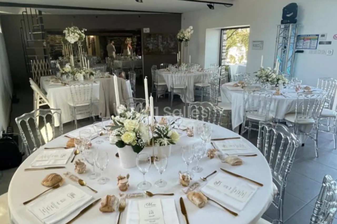 Salle de réception décorée pour un mariage, avec tables rondes dressées, nappes blanches et compositions florales élégantes.