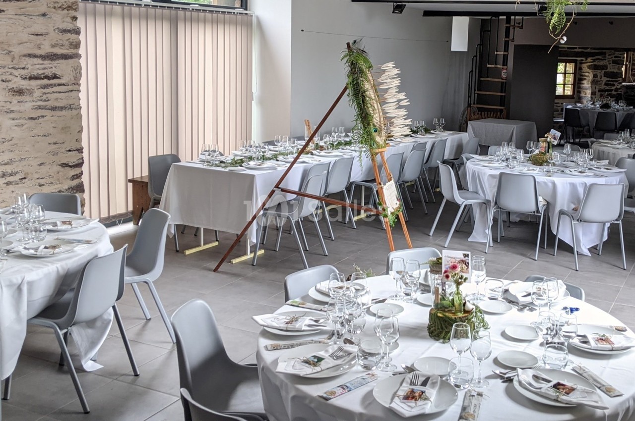 Salle de réception décorée pour un événement, avec des tables rondes dressées et des chaises grises.