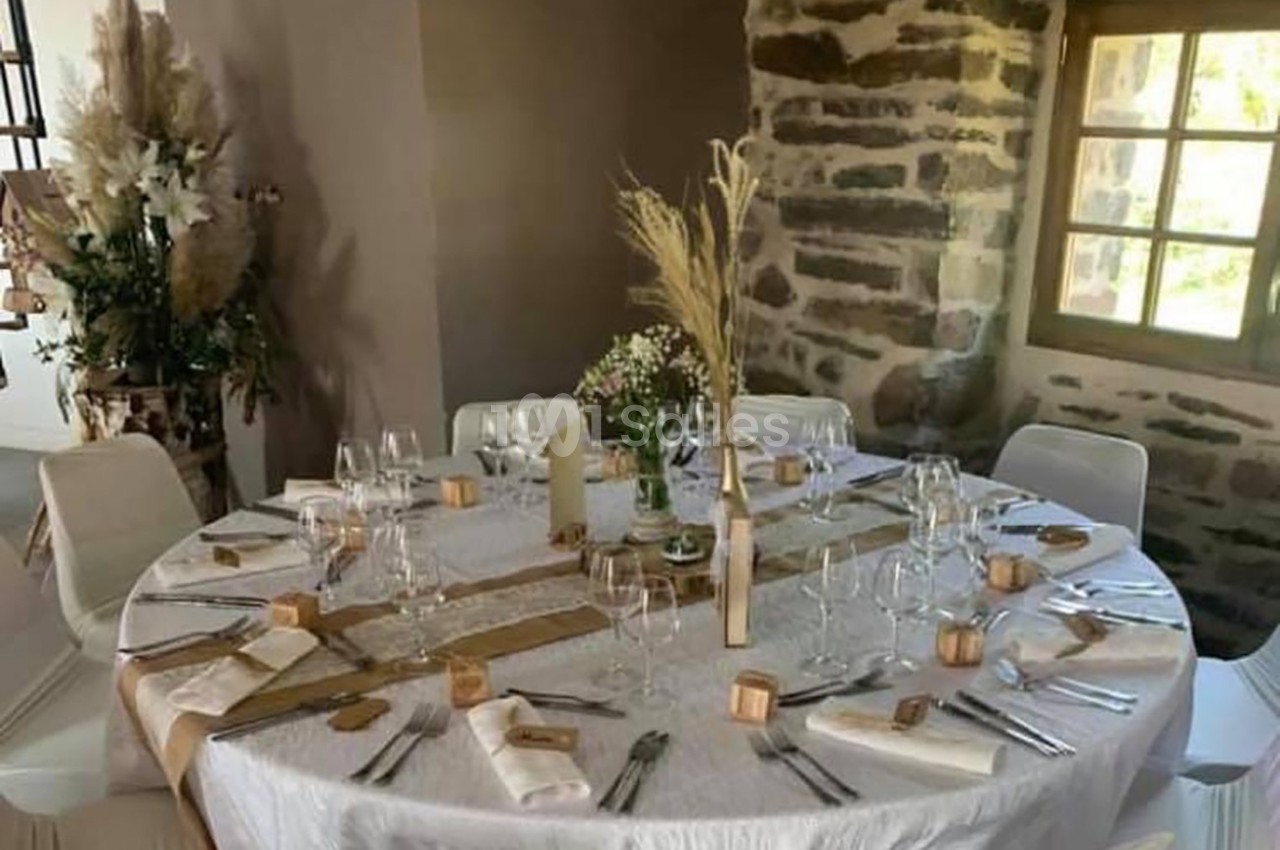 Table ronde décorée pour un repas, avec nappes blanches, couverts disposés, fleurs et éléments naturels en centre de table.
