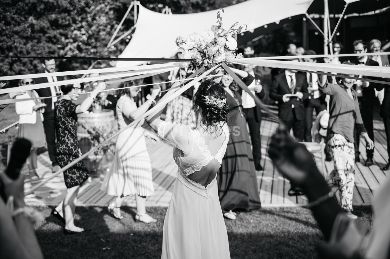 Une mariée danse en extérieur, entourée d'invités tenant des rubans, lors d'une célébration festive.