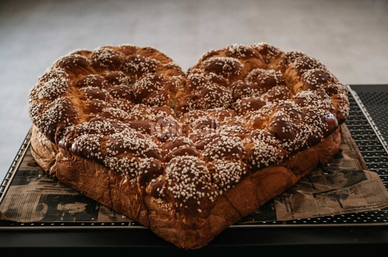 Brioche en forme de cœur, dorée et parsemée de sucre perlé, posée sur un plateau.