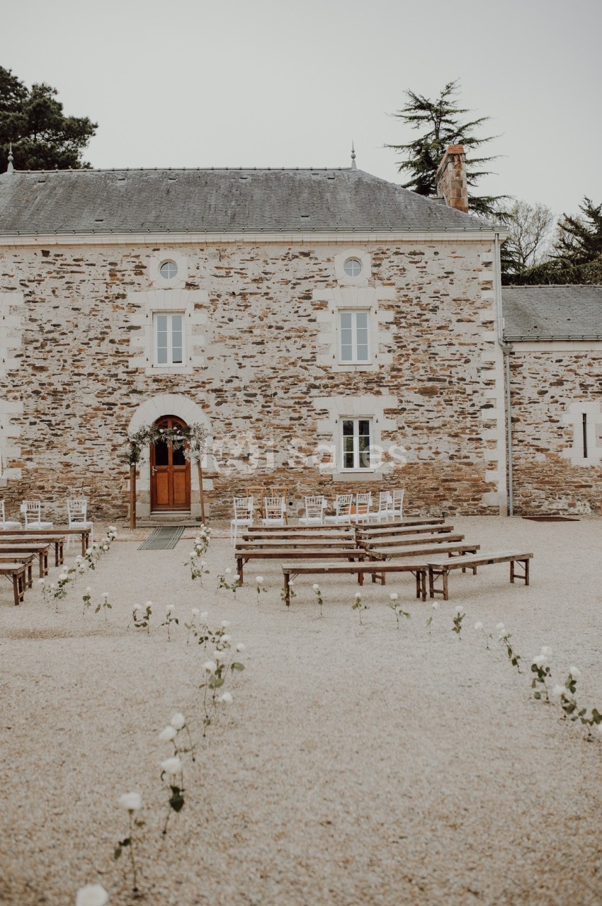 Façade en pierre d'un bâtiment ancien avec des bancs et des chaises disposés pour une cérémonie en extérieur.