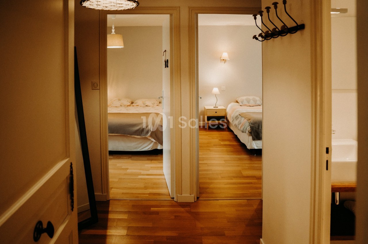 Vue d'un couloir menant à deux chambres avec lits doubles, éclairées par des lampes de chevet.