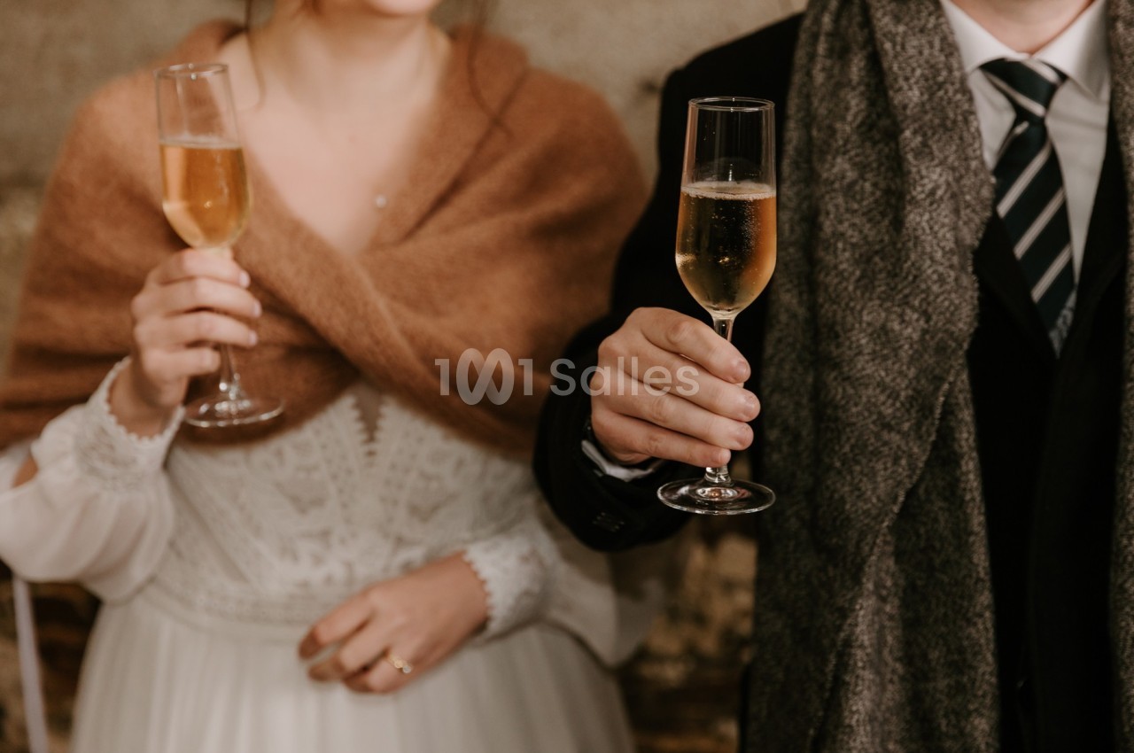 Un couple en tenue élégante tenant des flûtes de champagne dans un cadre chaleureux.