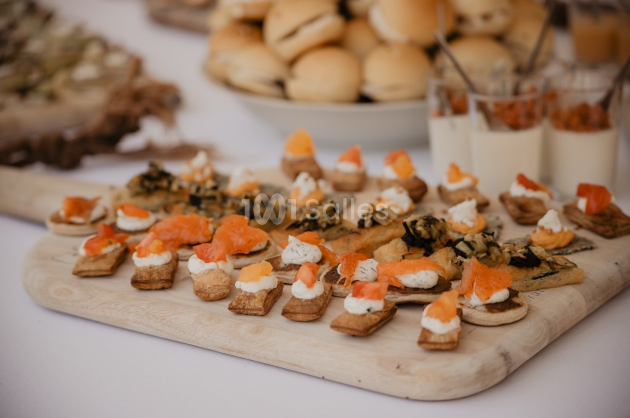Plateau de canapés variés avec saumon, fromage et garnitures, présenté sur une table lors d'un buffet.