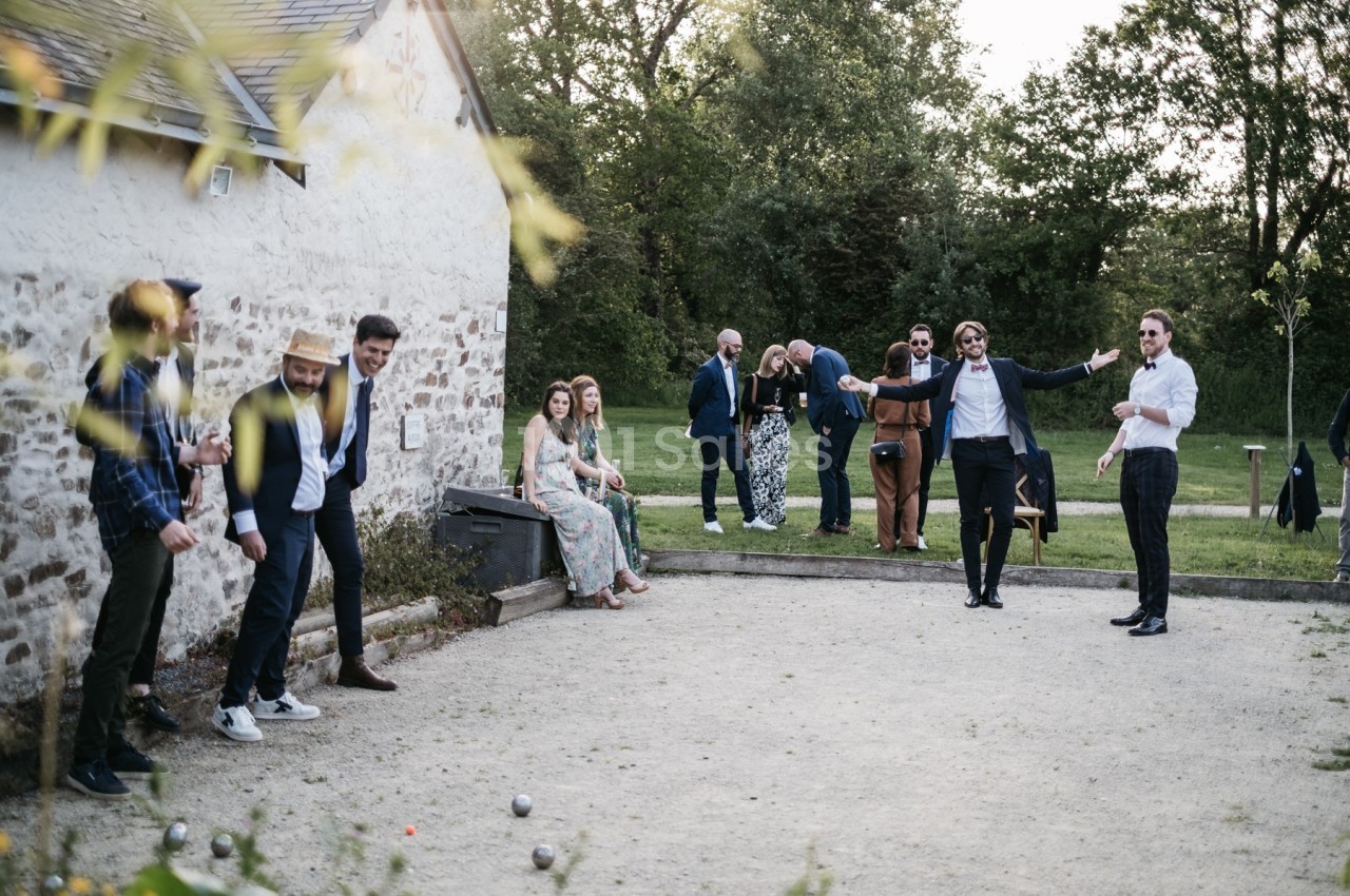 Des personnes jouent à la pétanque et discutent dans un espace extérieur près d'un bâtiment en pierre.
