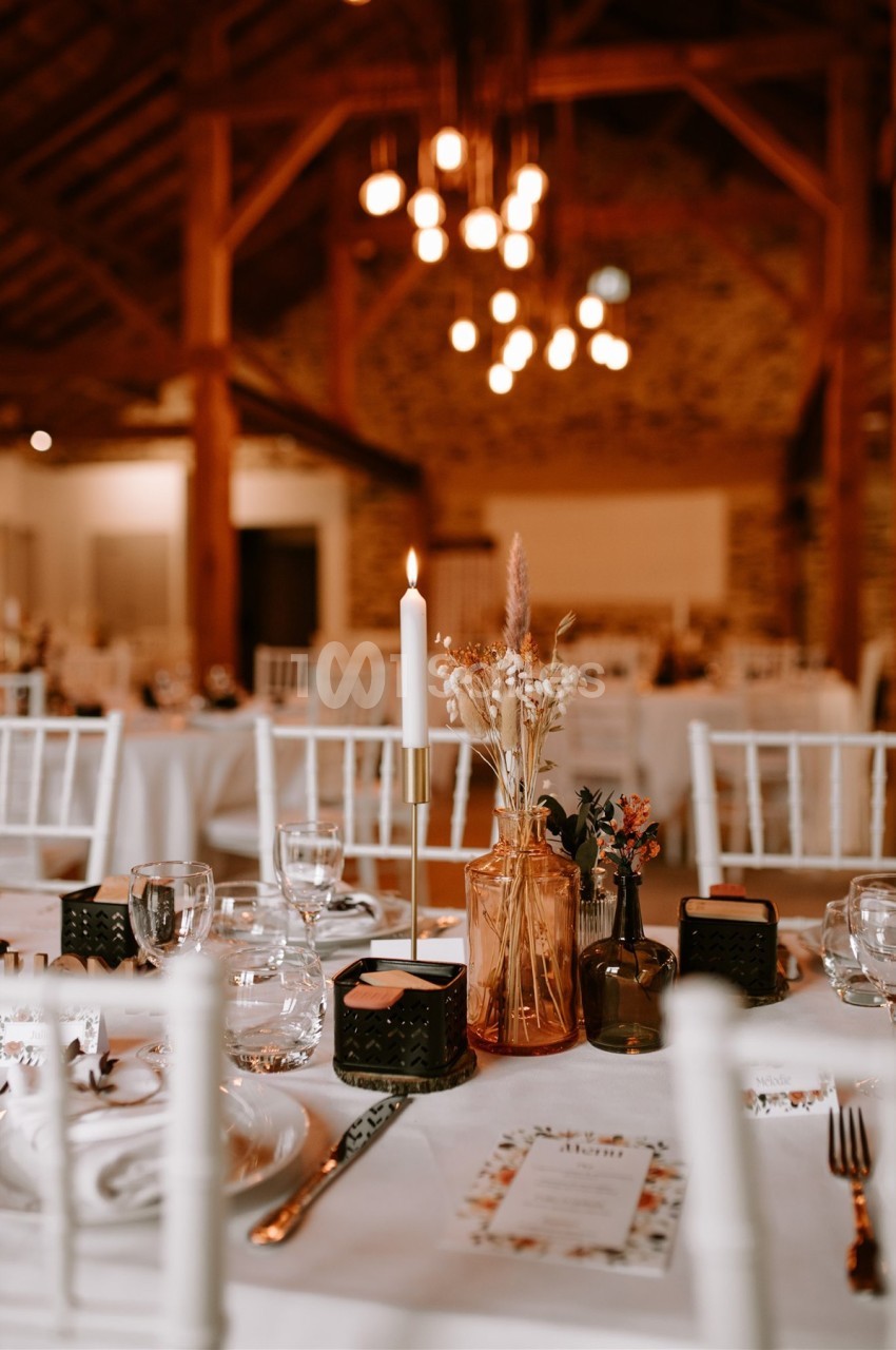 Salle de réception décorée avec des tables dressées, bougies allumées et fleurs séchées dans un cadre rustique.