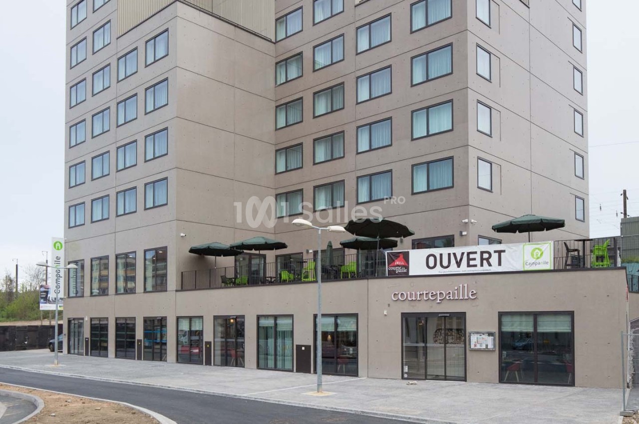 Façade d'un restaurant Courtepaille avec terrasse et enseigne ’OUVERT’, situé au rez-de-chaussée d'un immeuble moderne.