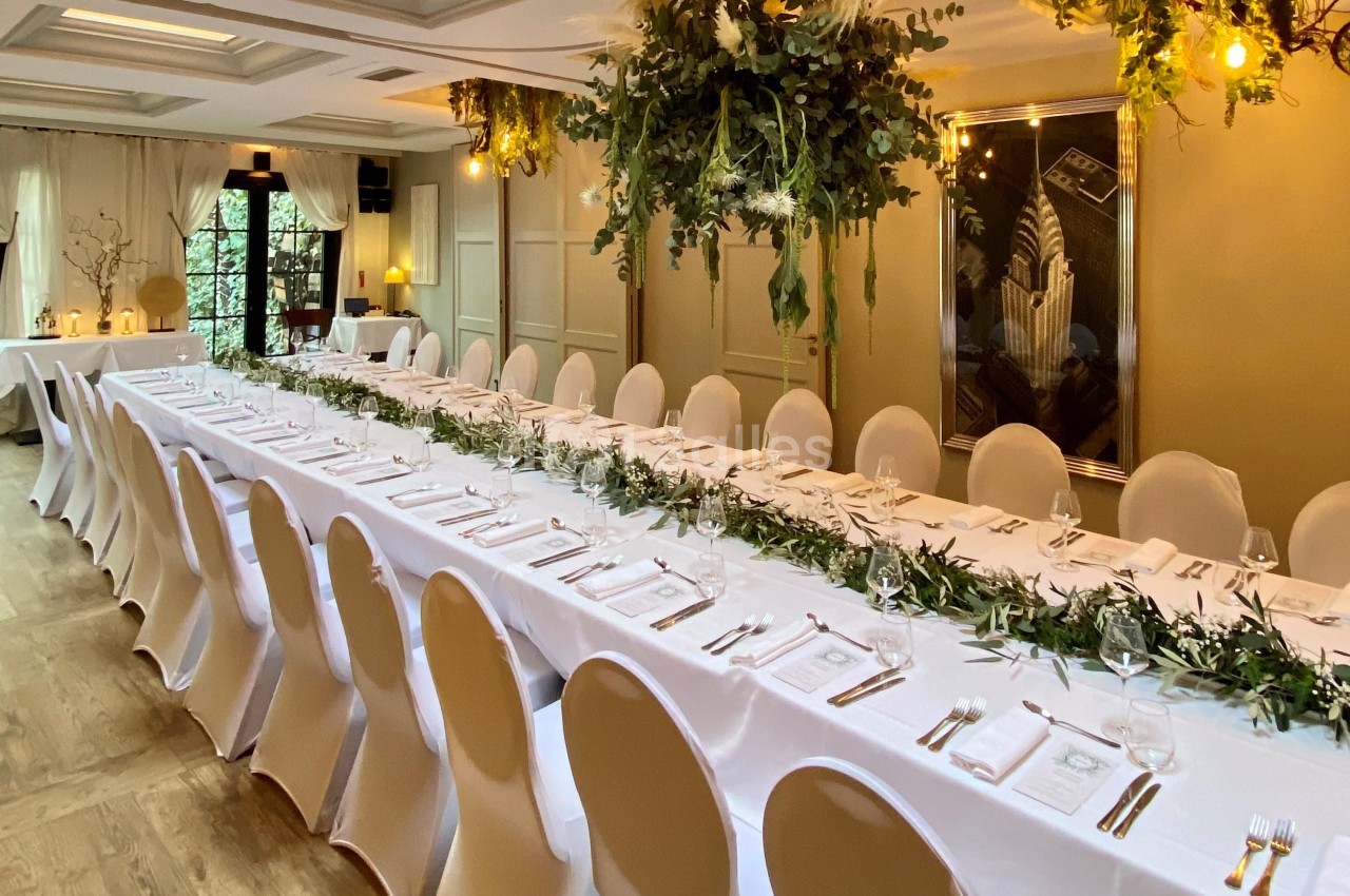 Salle de réception élégante avec une longue table dressée, décorée de feuillages et de suspensions végétales.