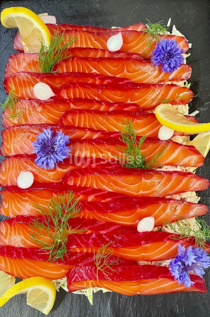 Tranches de saumon gravlax rouge vif garnies d'aneth, fleurs bleues, rondelles de citron et touches de crème blanche.