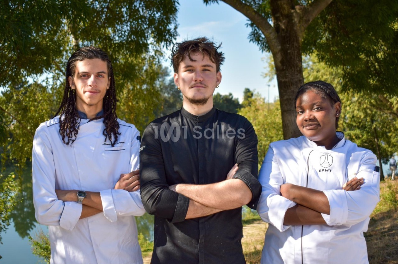 Trois professionnels posent ensemble sous les arbres en bordure d'eau, vêtus de tenues blanches et noires.