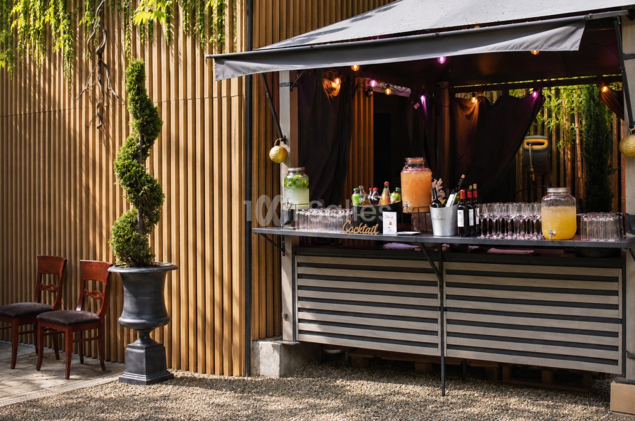 Bar de cocktails extérieur avec comptoir dressé, lumières multicolores et chaises hautes en bois.