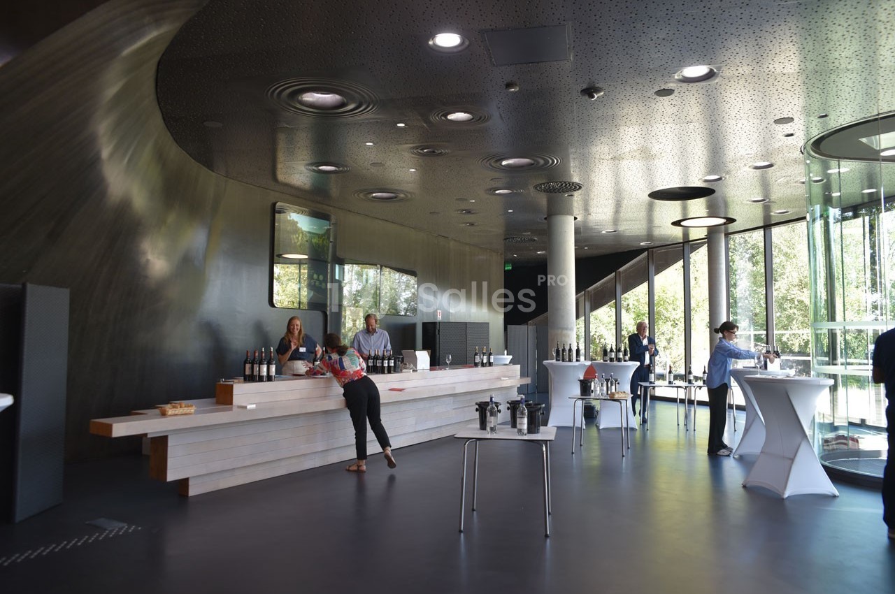 Un espace moderne avec un comptoir de dégustation de vins, des tables hautes et de grandes baies vitrées donnant sur l…