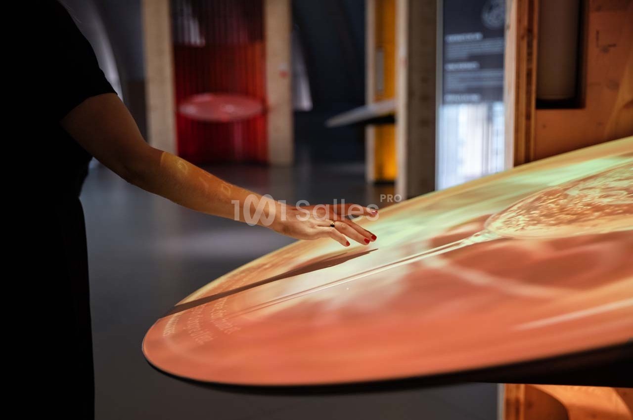 Une main touche une surface interactive lumineuse dans un espace intérieur moderne.