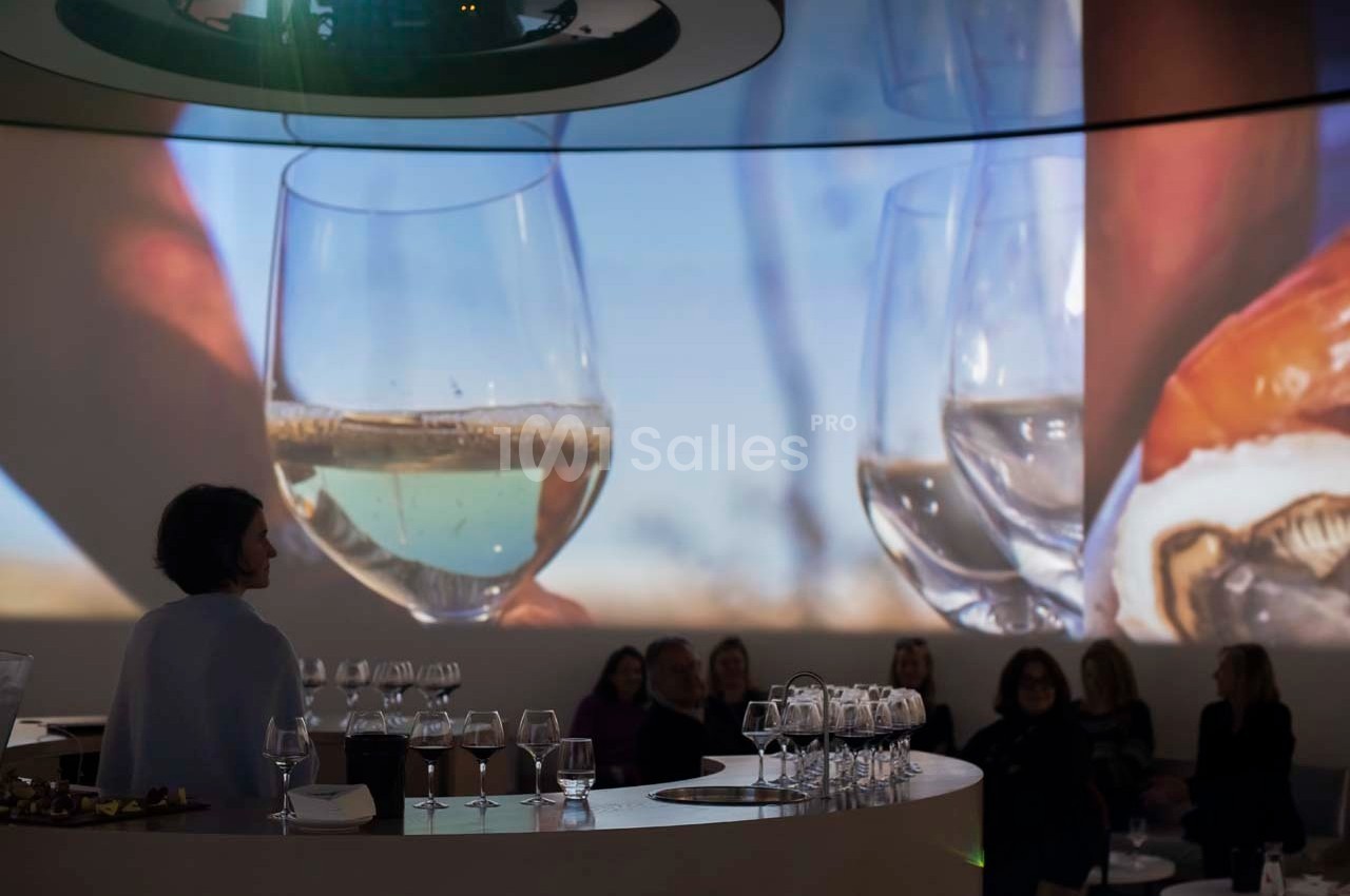 Des personnes assises dans une salle sombre avec des projections de verres de vin et d'huîtres en arrière-plan.