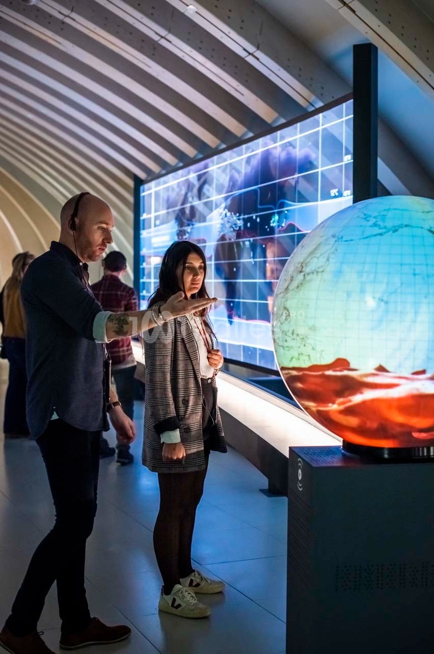 Un homme et une femme observent un globe interactif illuminé dans un espace d'exposition moderne.