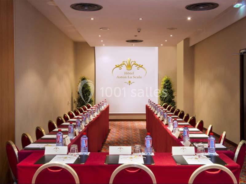 Salle de réunion aménagée avec des tables en U, chaises rouges, bouteilles d'eau et blocs-notes, éclairage tamisé.