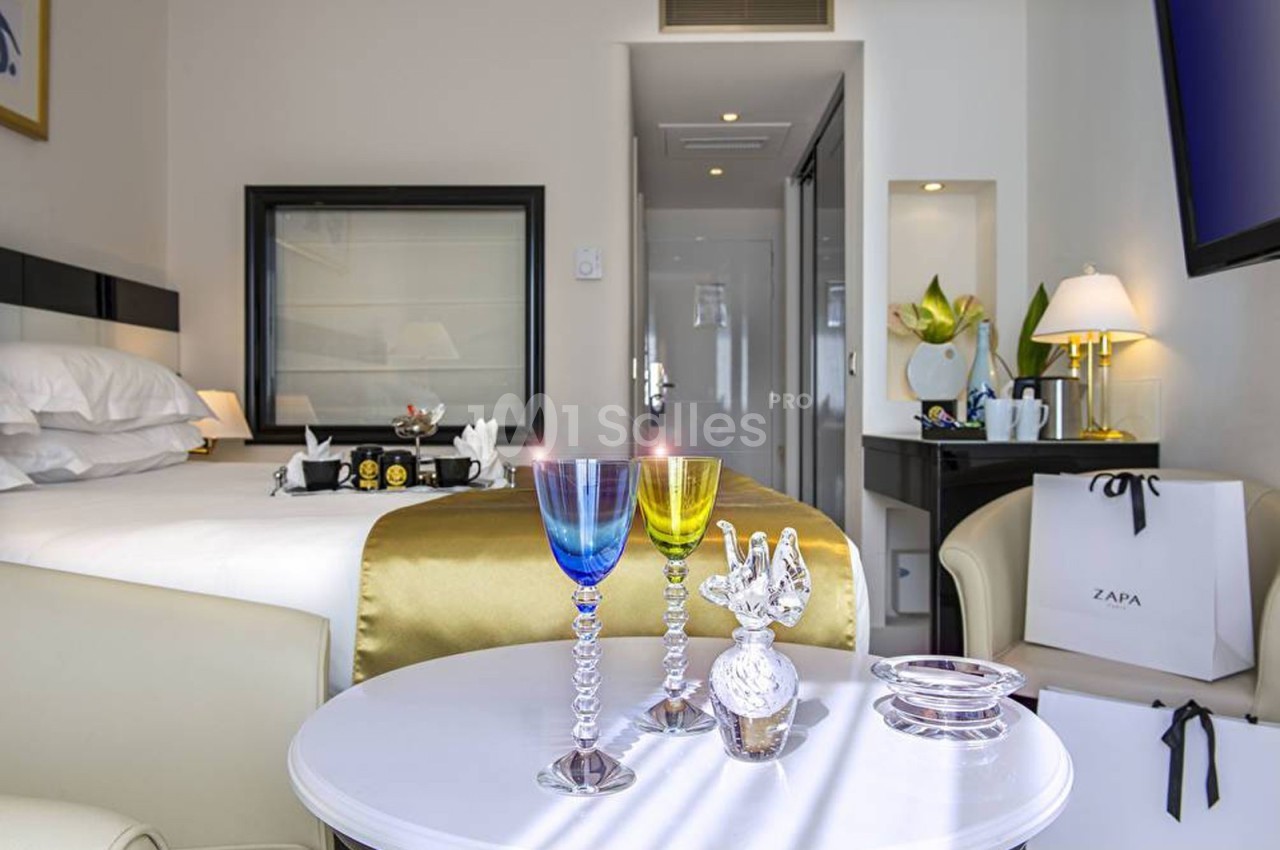 Chambre d'hôtel lumineuse avec lit double, table ronde ornée de verres colorés et décoration élégante.