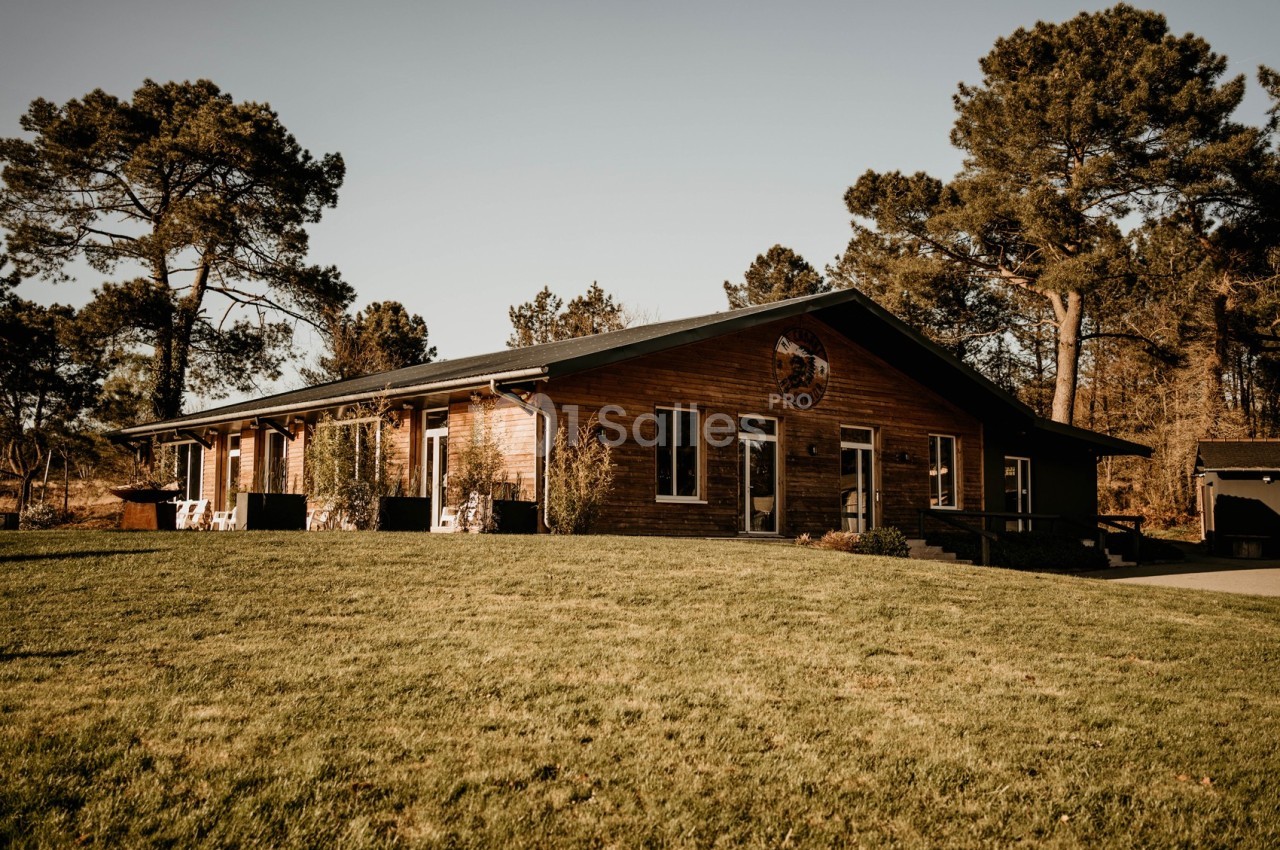 Bâtiment en bois de plain-pied entouré d'arbres, avec une pelouse verdoyante au premier plan.
