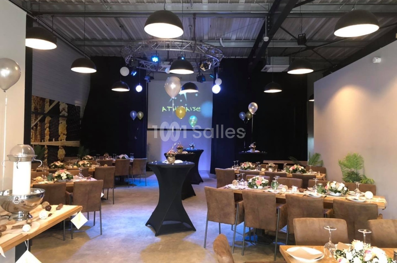Salle de réception décorée avec des tables dressées, des ballons et un éclairage tamisé sous un plafond industriel.
