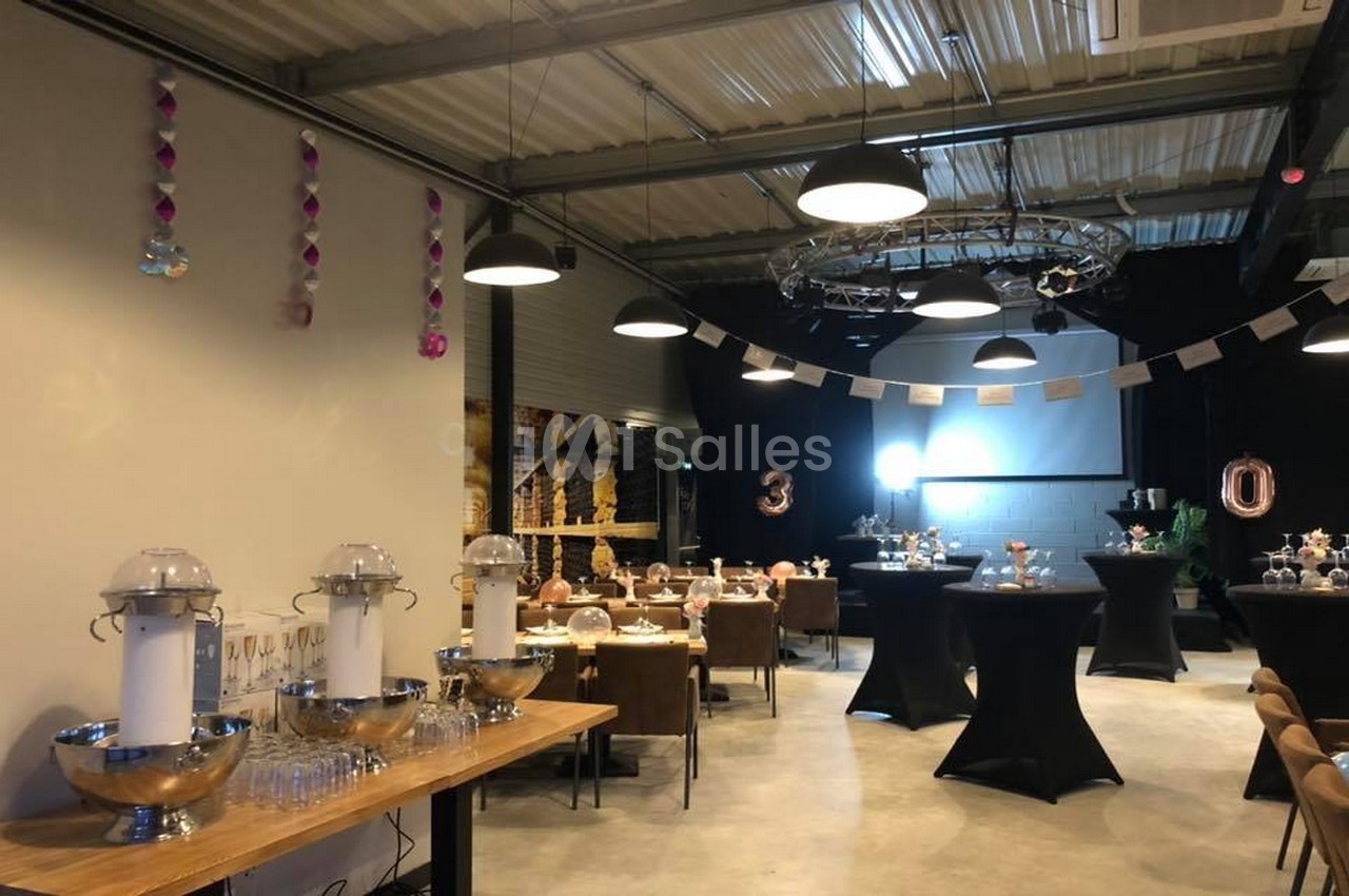 Salle décorée pour une fête avec tables dressées, guirlandes suspendues et chiffres ’30’ en arrière-plan.