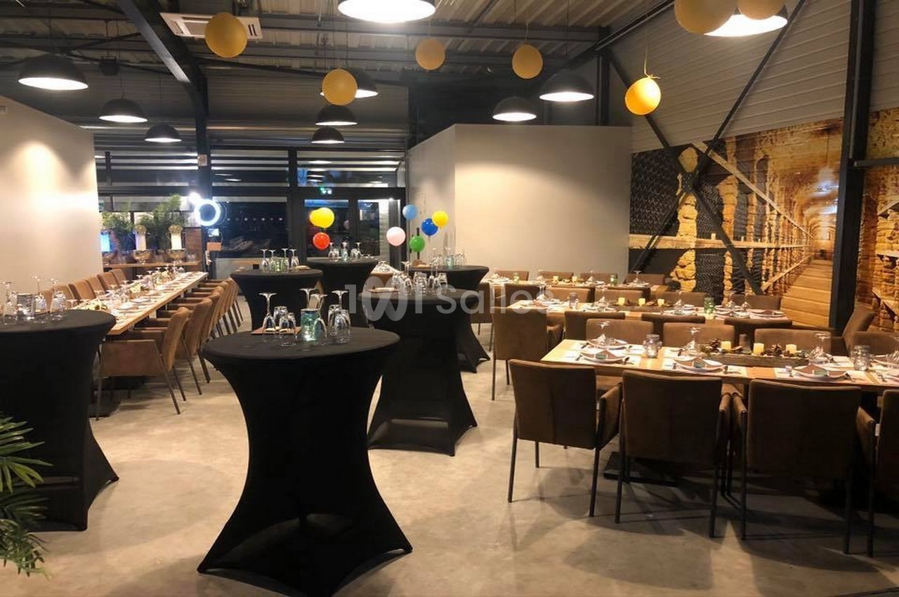 Salle de réception décorée avec des tables dressées, des ballons colorés et des tables hautes noires.