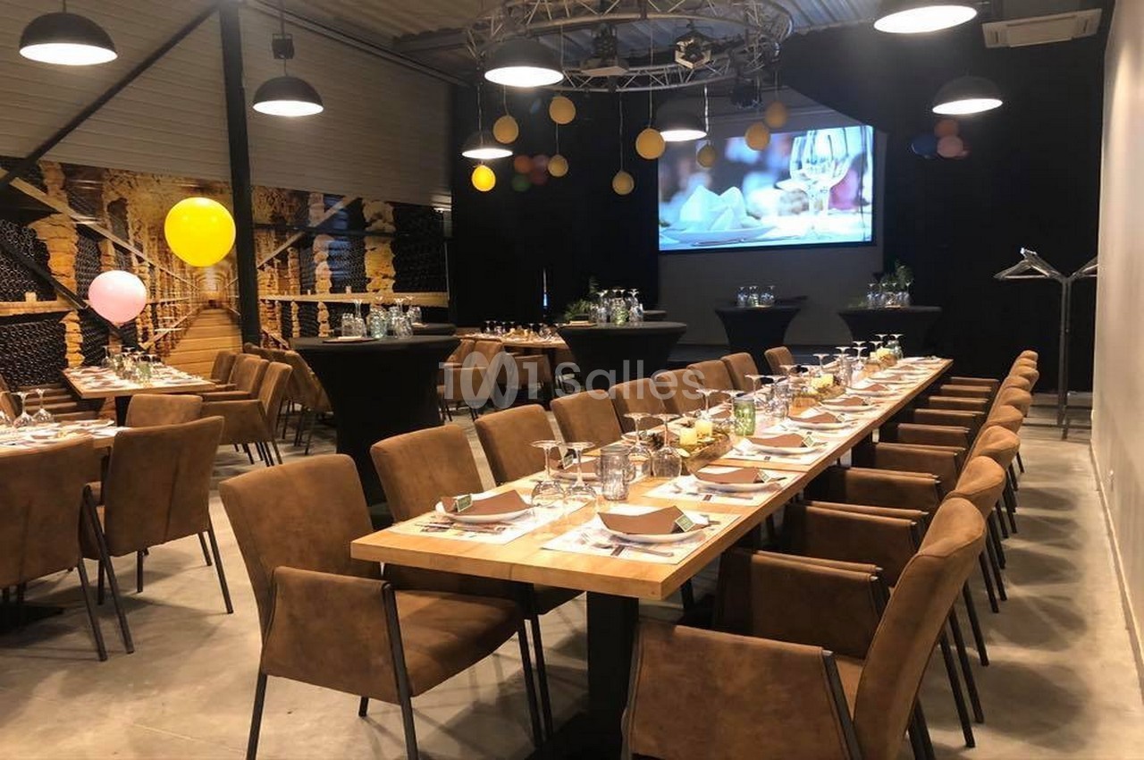 Salle de réception décorée avec des tables dressées, des chaises en cuir marron et des ballons colorés suspendus.