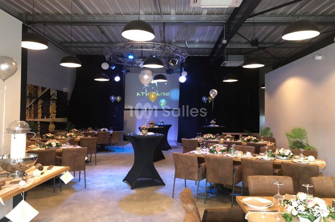Salle de réception décorée avec des tables dressées, des ballons et un éclairage tamisé sous un plafond industriel.