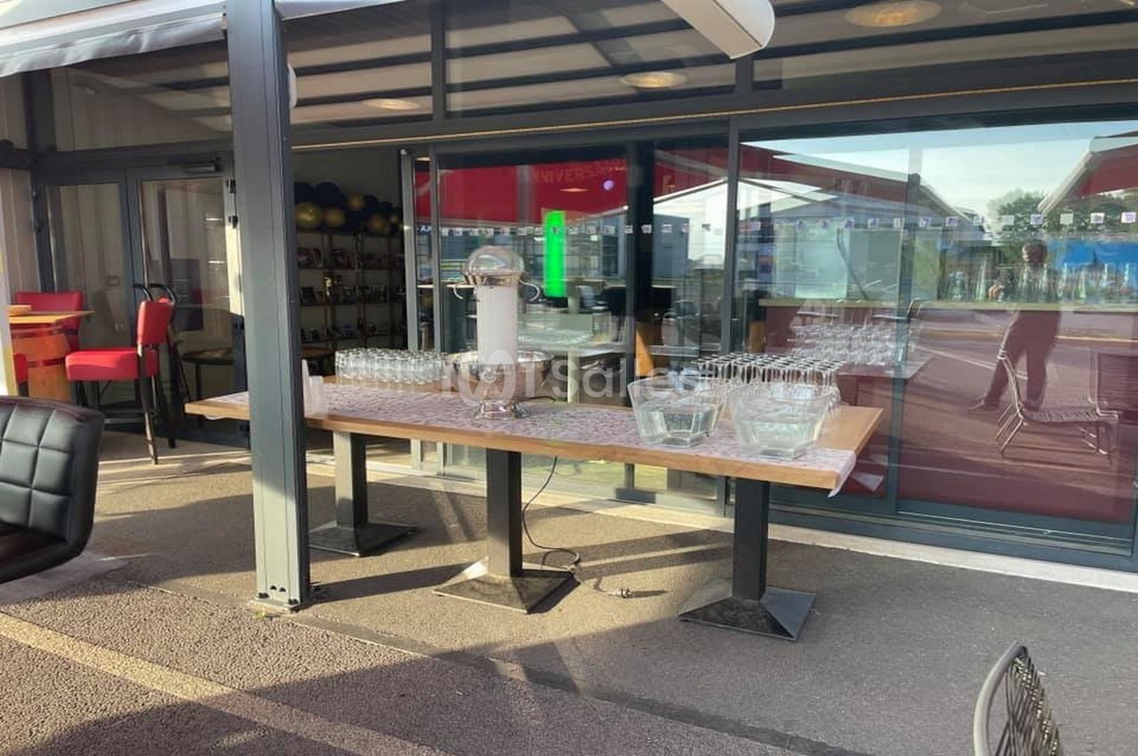 Table en extérieur avec verres alignés et seau à glaçons, située près d'une baie vitrée d'un espace couvert.