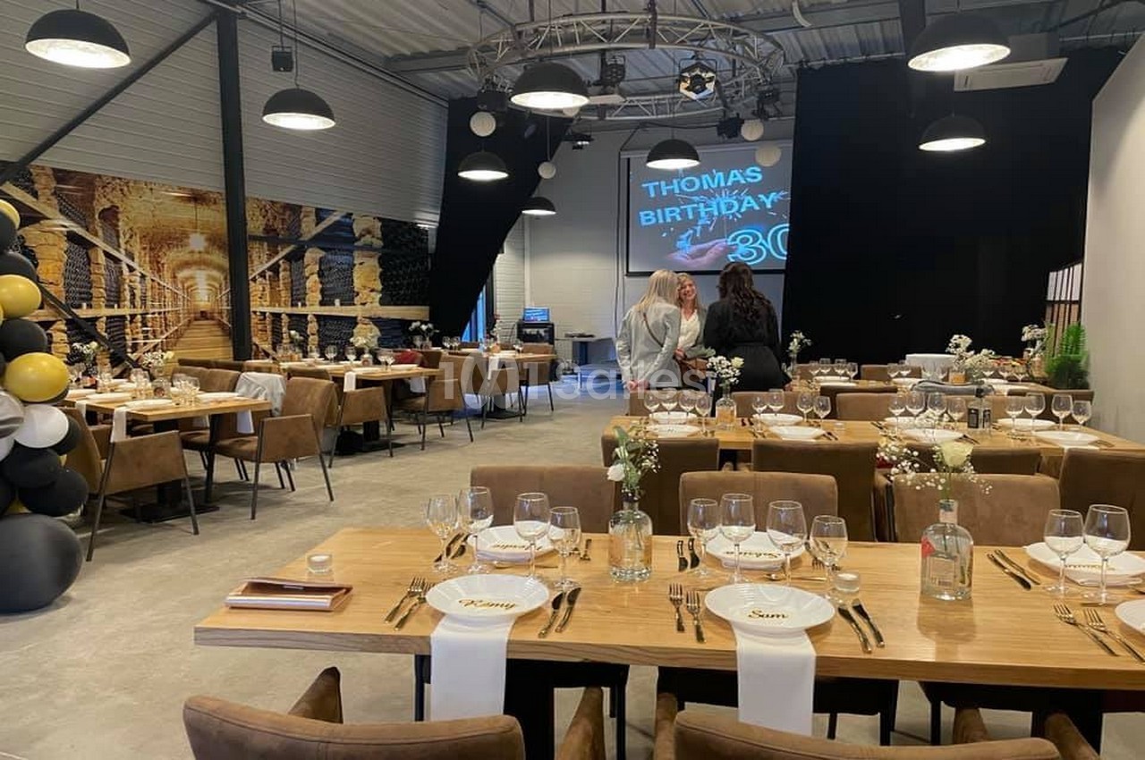 Salle décorée pour un anniversaire avec tables dressées, ballons noirs et dorés, et écran affichant ’Thomas Birthday 30’.