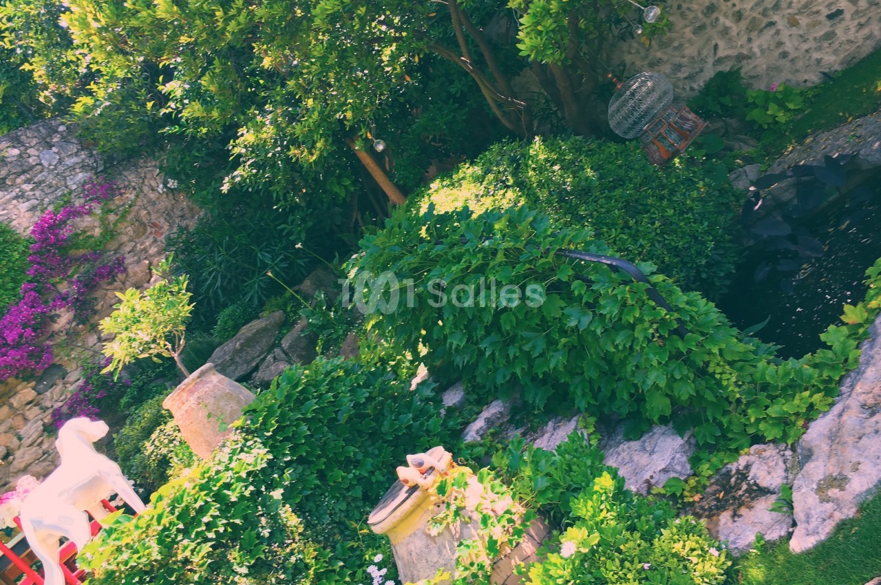 Jardin verdoyant avec pierres, arbustes, fleurs colorées et petit bassin entouré de végétation.