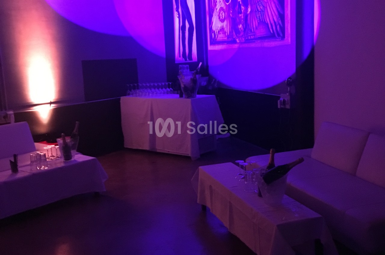 Salle faiblement éclairée avec canapés, tables dressées et décorations murales sous des lumières violettes.