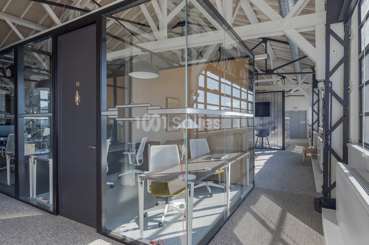 Bureau vitré moderne avec deux postes de travail, situé dans un espace lumineux avec poutres apparentes.