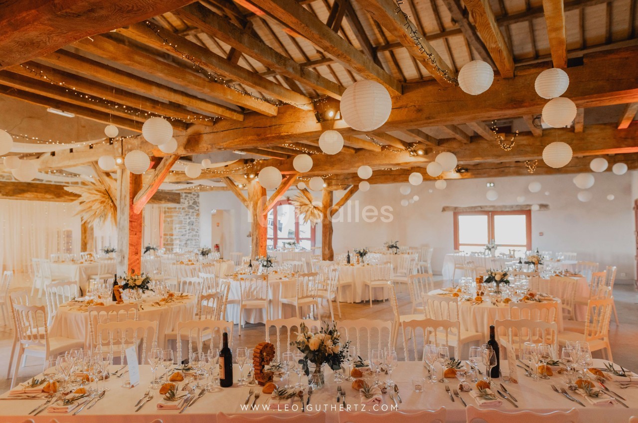 Salle de réception décorée pour un mariage, avec tables dressées, guirlandes lumineuses et lanternes suspendues.