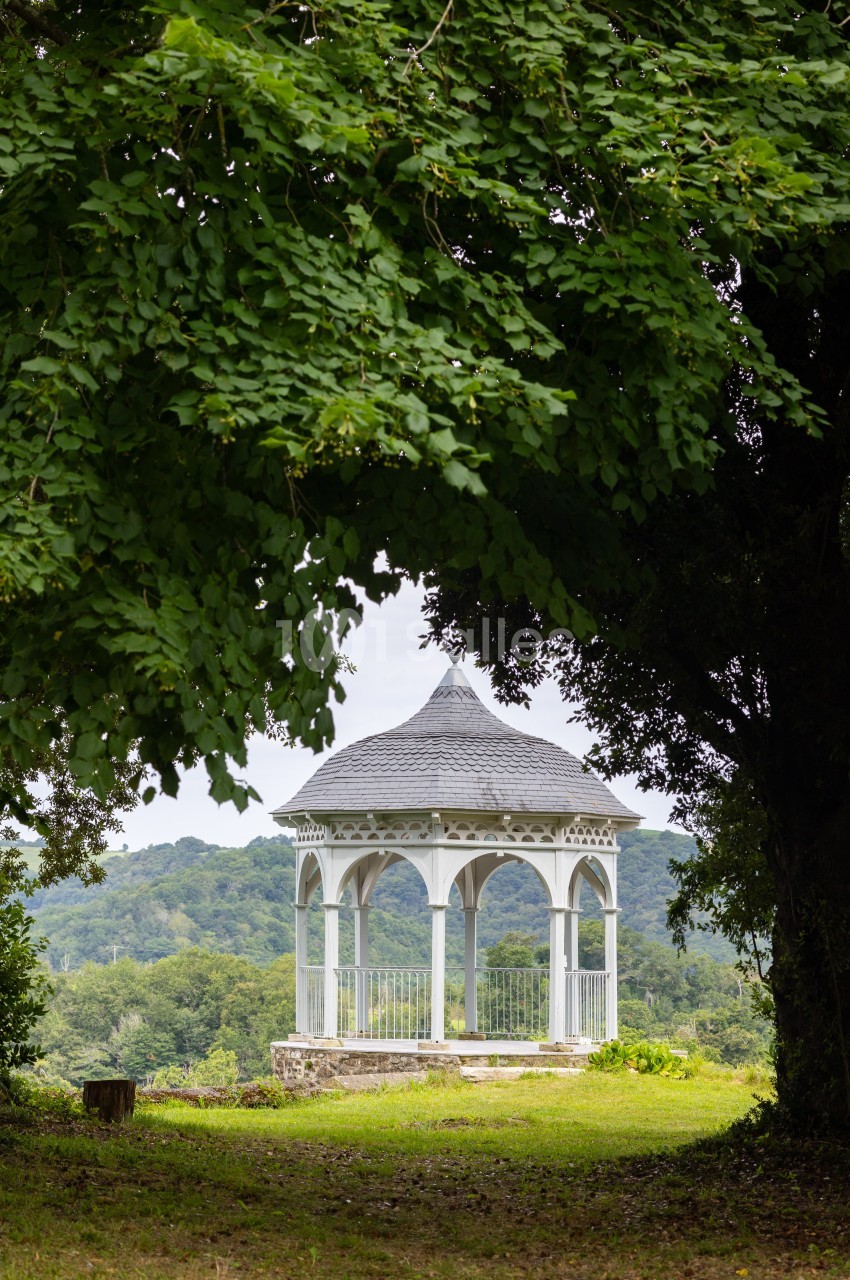 Kiosque blanc en bois au toit arrondi, entouré de verdure, avec une vue dégagée sur des collines boisées.