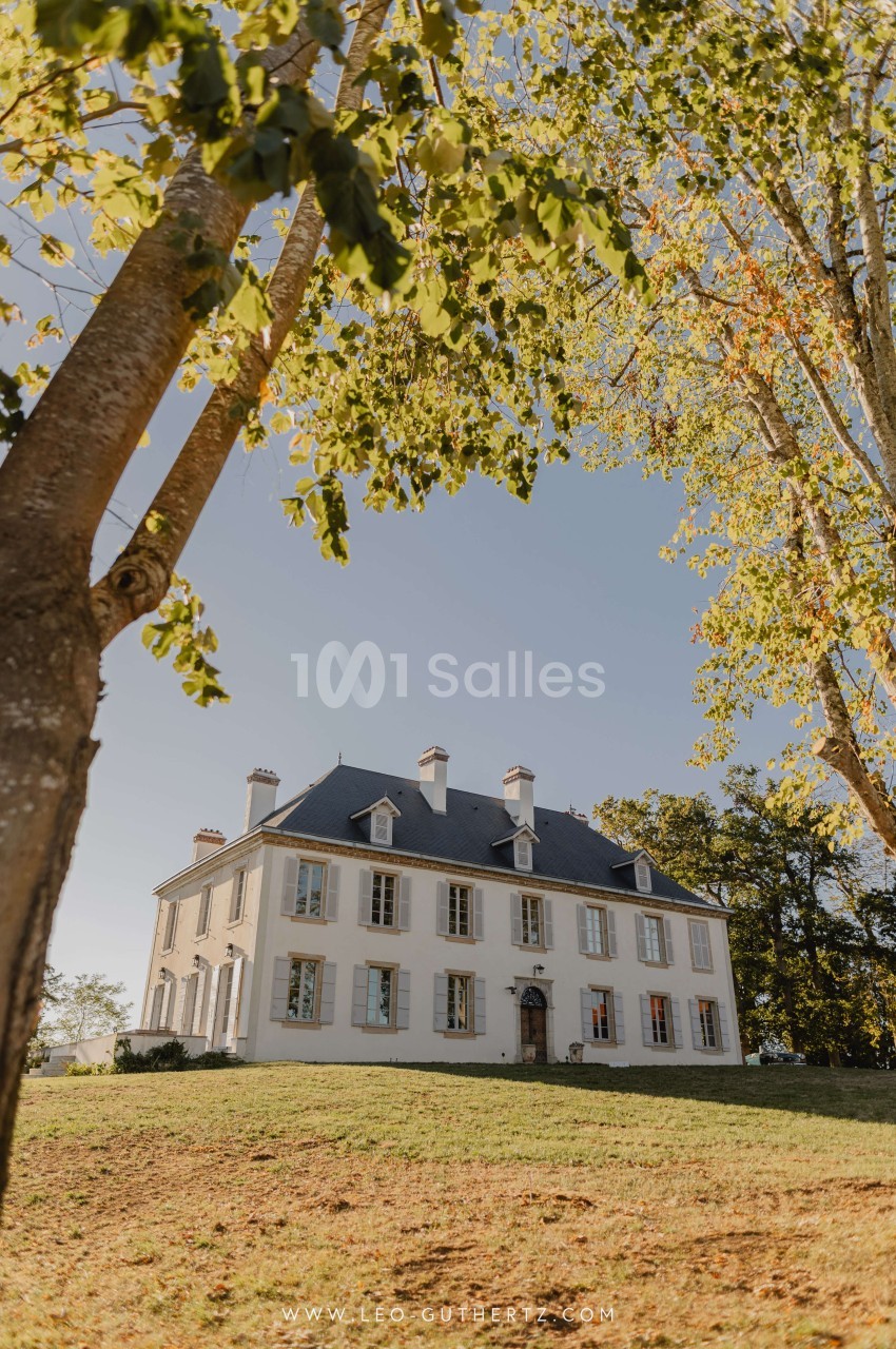 Façade d'un manoir blanc entouré d'arbres, situé sur une pelouse sous un ciel dégagé.