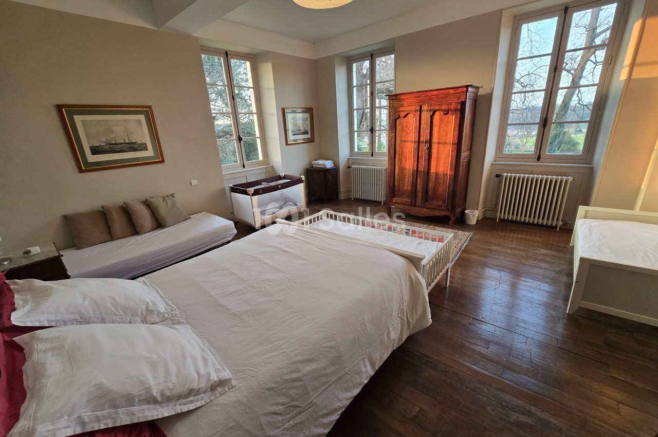 Chambre lumineuse avec lit double, lit bébé, armoire en bois, canapé et grandes fenêtres donnant sur l'extérieur.
