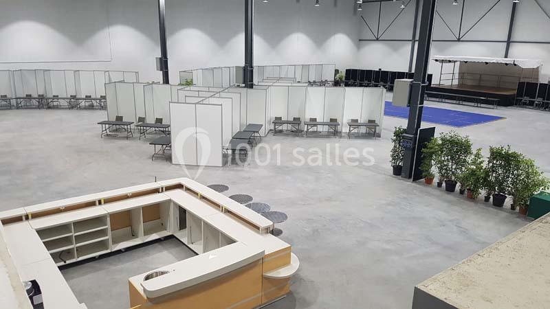 Salle spacieuse aménagée avec des cloisons, des bancs, des plantes en pot et une scène au fond.