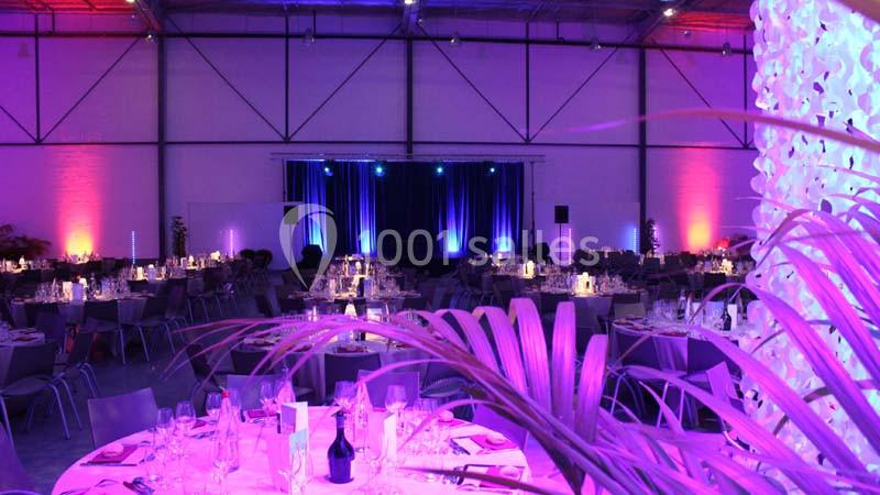 Salle de réception décorée avec des éclairages violets, tables dressées et scène éclairée en arrière-plan.