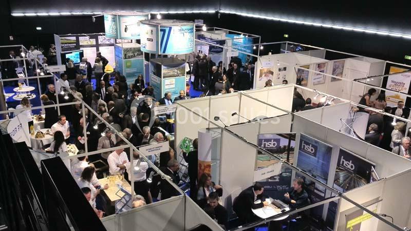 Vue aérienne d'un salon professionnel avec des stands, des visiteurs et des échanges entre participants.
