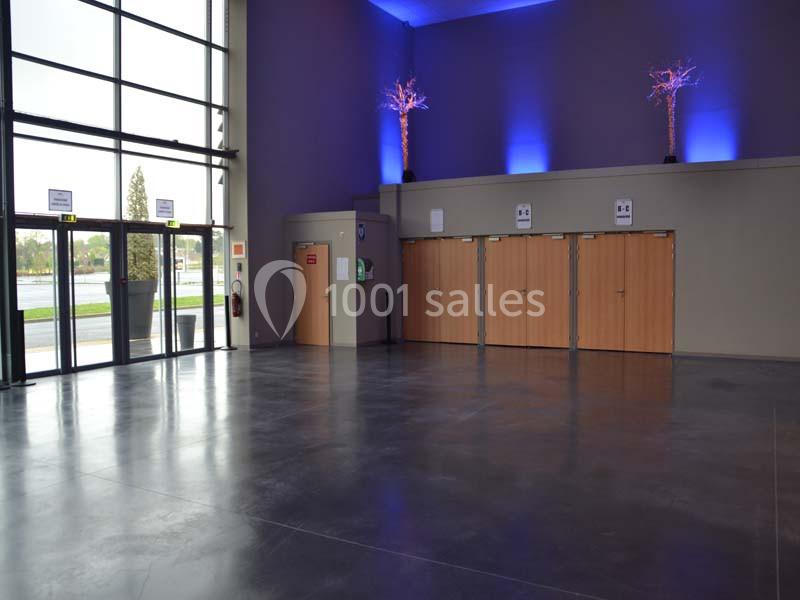Hall d'entrée spacieux avec sol en béton, portes en bois, grandes fenêtres et éclairage bleu décoratif.