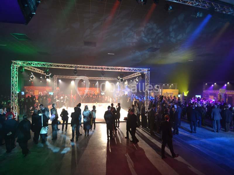Salle de réception éclairée avec des projecteurs colorés, des invités rassemblés autour d'une piste centrale.