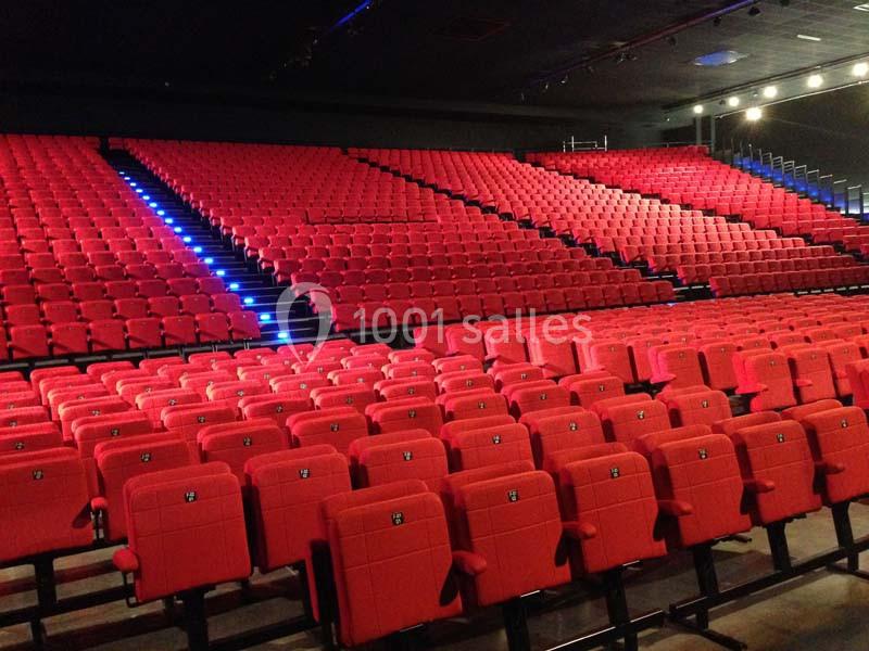 Salle de spectacle avec de nombreuses rangées de sièges rouges vides et un éclairage discret.