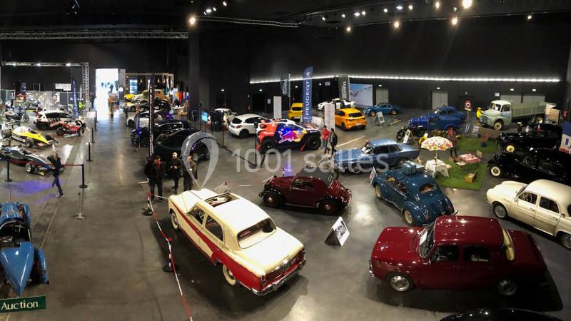 Vue d'une exposition intérieure de voitures anciennes et modernes, avec des visiteurs observant les véhicules.