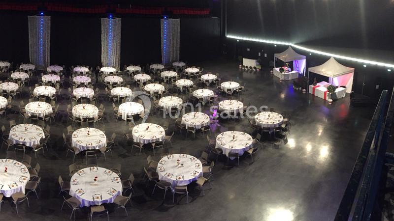 Salle de réception avec de nombreuses tables rondes dressées et un espace traiteur sous des tentes blanches.