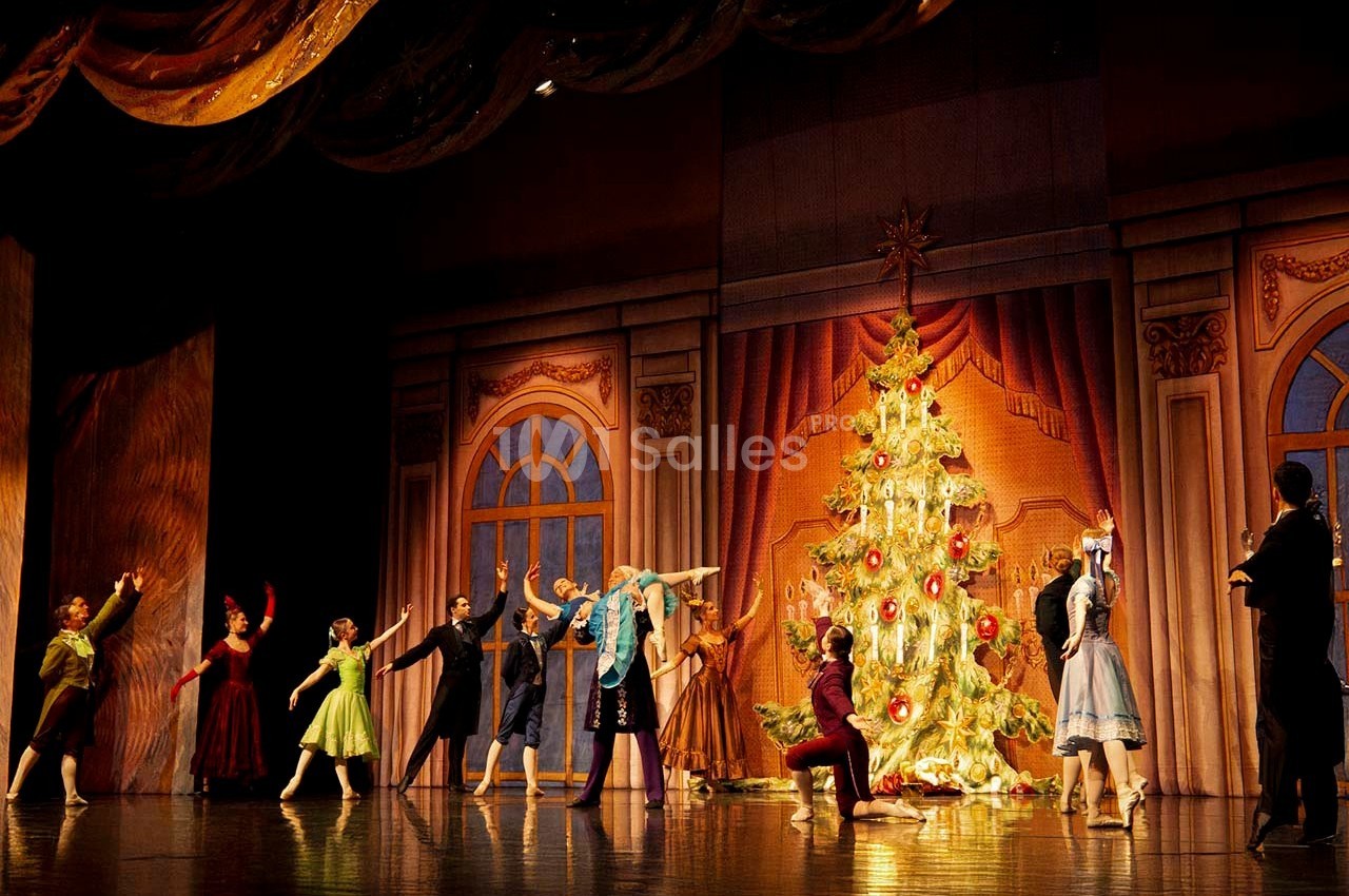 Des danseurs en costume exécutent une scène de ballet devant un grand sapin de Noël décoré sur une scène de théâtre.