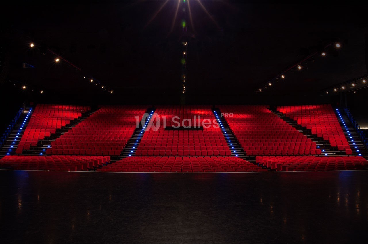 Salle de spectacle vide avec rangées de sièges rouges et éclairage tamisé, escalier central illuminé.