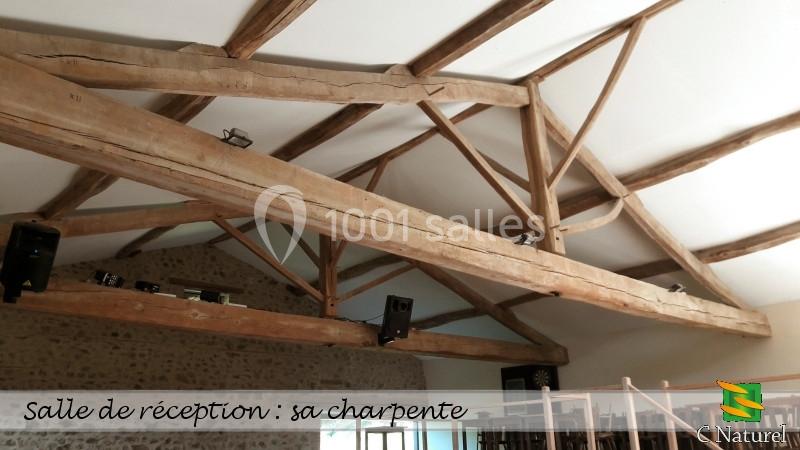 Charpente en bois apparente d'une salle de réception avec murs en pierre et plafond blanc.